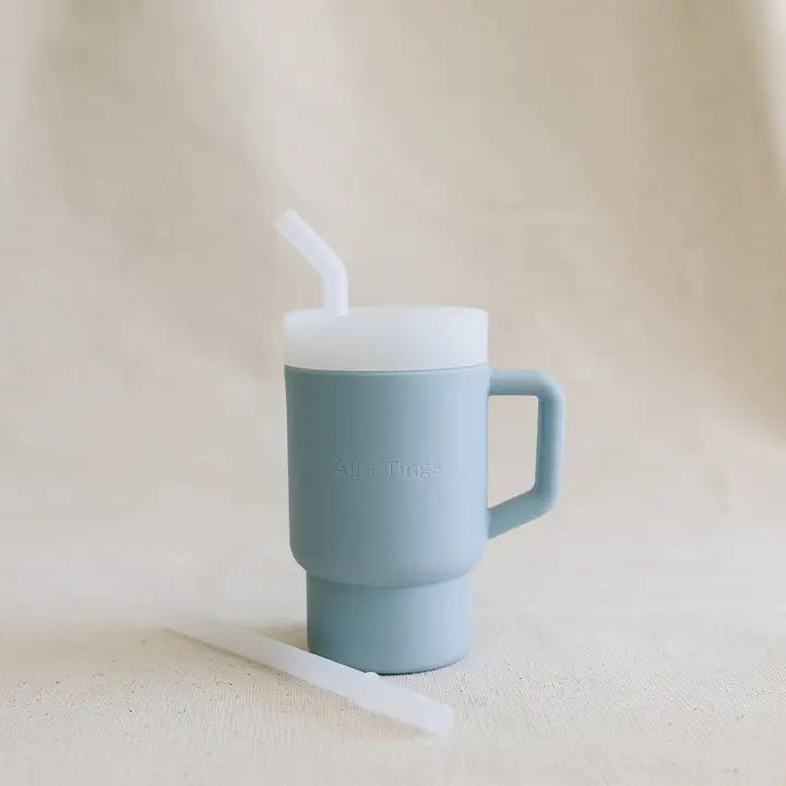 Blue mug with a white lid and straw on a beige background
